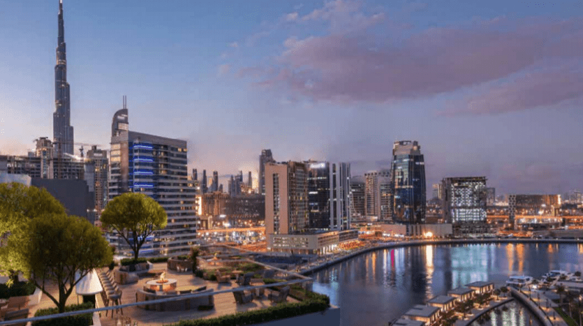 Vue panoramique sur les toits d'une ville moderne au crépuscule, avec le Burj Khalifa et d'autres gratte-ciel illuminés, avec une rivière réfléchissante et un ciel clair, vu du 15e