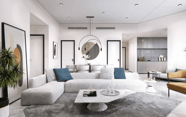 Un salon moderne comprenant un canapé sectionnel blanc avec des coussins bleus, un miroir circulaire au mur et une cuisine ouverte en arrière-plan. Décor aux tons neutres et plante en pot du 15