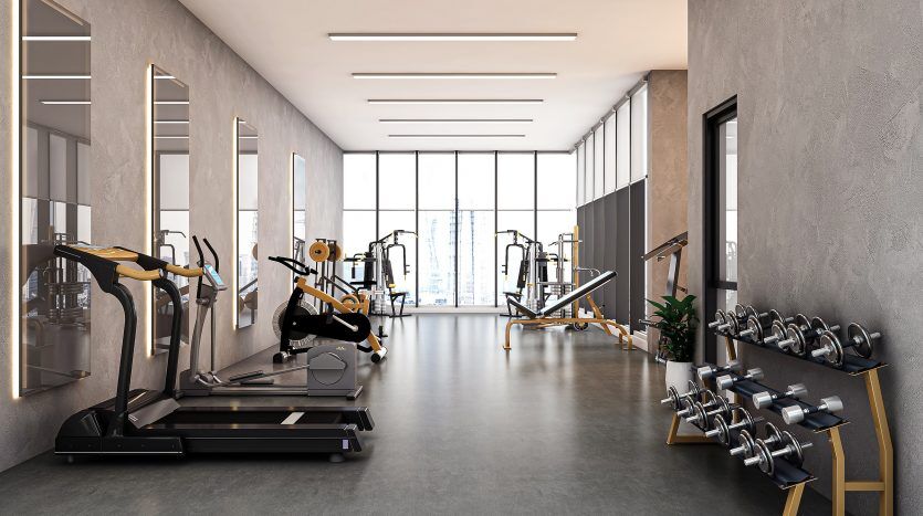 Une salle de sport moderne au Prime Residency 3 avec de grandes fenêtres laissant entrer la lumière naturelle, comprenant des tapis roulants, des machines elliptiques et un rack d'haltères, le tout organisé dans un espace propre et propre.