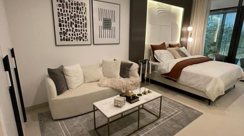 Une chambre moderne et minimaliste dans Prime Residency 3 avec une palette de couleurs neutres avec un canapé sectionnel moelleux, un lit élégant avec une literie impeccable, des œuvres d'art murales abstraites et une table basse en verre sur