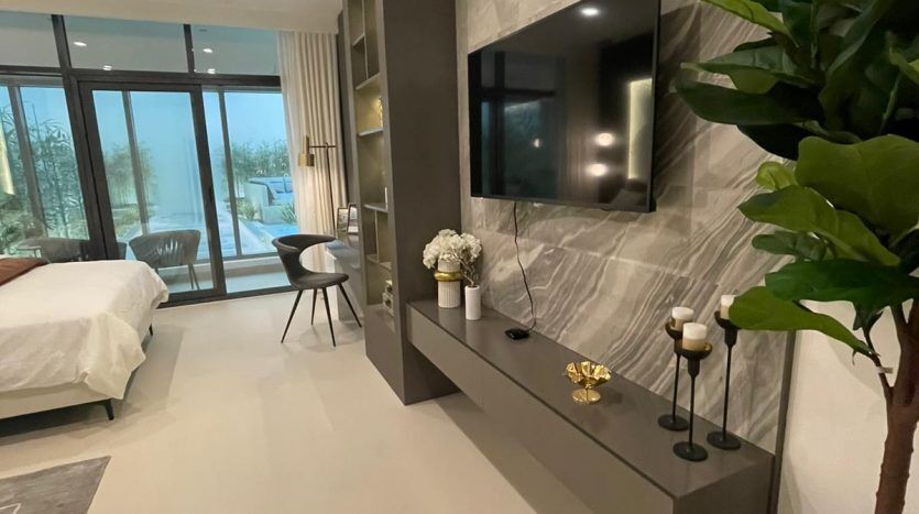 Une chambre d'hôtel moderne dans Prime Residency 3 au design épuré, comprenant un grand lit, une télévision murale sur un mur en marbre, un bureau et une plante en pot, avec sol