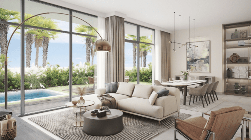 Salon moderne à Al Furjan avec de grandes fenêtres donnant sur une piscine et une verdure luxuriante à l'extérieur. Comprend un canapé sectionnel beige, une table basse ronde et un coin repas en arrière-plan. Lumineux et aéré