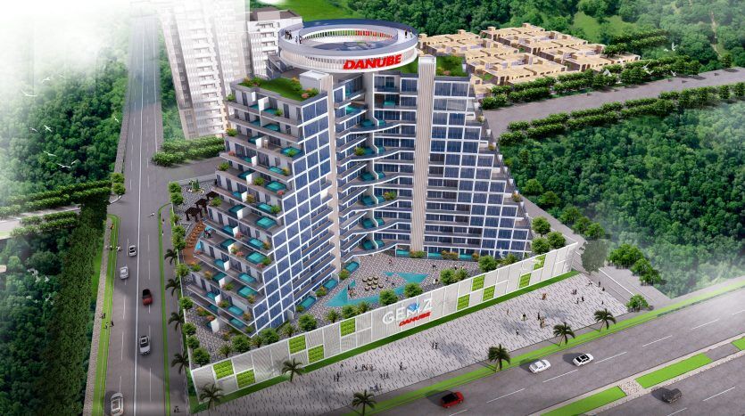 Vue aérienne d'un immeuble d'appartements moderne à plusieurs étages à Dubaï avec des balcons en verre teinté bleu, entouré d'une verdure luxuriante et adjacent à une rue avec des voitures en mouvement. Le bâtiment présente des caractéristiques proéminentes