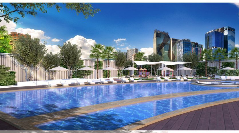 Espace piscine luxueux avec chaises longues et parasols, entouré d'arbres tropicaux et d'immeubles modernes de grande hauteur sous un ciel bleu clair, disponible via notre agenceimmobilière Dubaï.