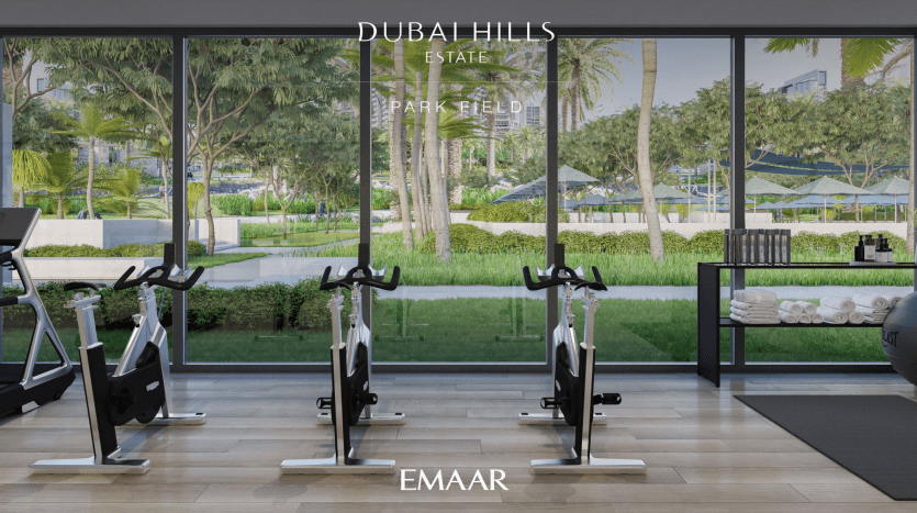 Une salle de sport moderne avec de grandes fenêtres donnant sur la verdure luxuriante du Dubai Hills Park. Des vélos d'exercice au premier plan et des vues sereines sur l'extérieur améliorent l'atmosphère d'entraînement, idéale pour ceux qui s'intéressent à l'investissement à Dubaï.