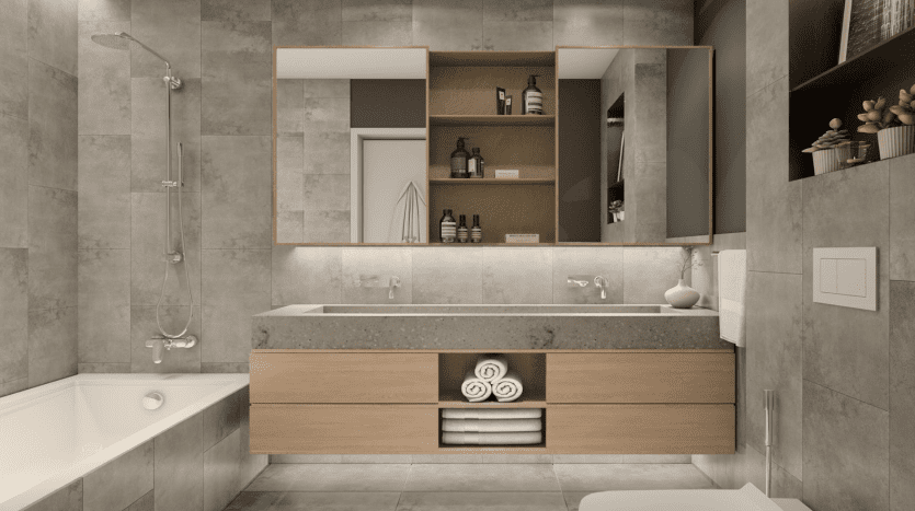 Salle de bain moderne dans un appartement de Dubaï avec un grand miroir, un meuble double vasque avec armoires en bois, une douche à l'italienne à gauche et une baignoire, le tout sur des murs et un sol carrelés gris.