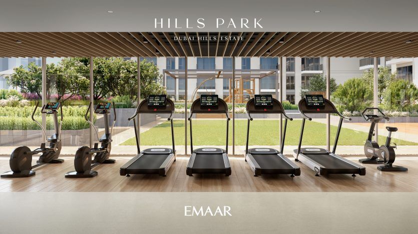 Salle de sport moderne avec tapis roulants et rameurs faisant face à de grandes fenêtres donnant sur un parc serein, sous un élégant plafond en bois, située à Hills Park, Dubai Hills Estate par une agence immobilière renommée.