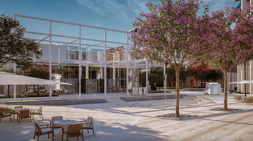 Une place extérieure moderne avec un bâtiment en verre, des arbres roses en fleurs et des coins salons sous des parasols blancs, avec un ciel dégagé. La lumière du soleil baigne le sol soigneusement carrelé et l'architecture contemporaine, parfaite