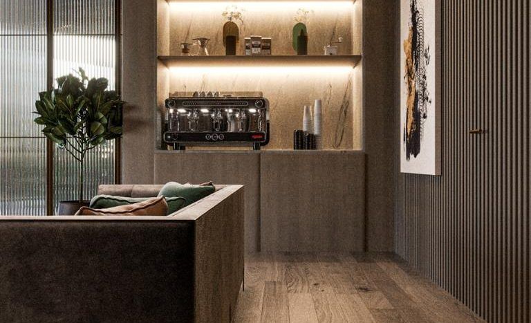 Un intérieur de cuisine élégant dans un appartement de Dubaï comprenant un îlot en béton avec un coussin vert, un parquet et des étagères éclairées présentant des vases et une machine à café. Une œuvre d’art encadrée est accrochée au mur