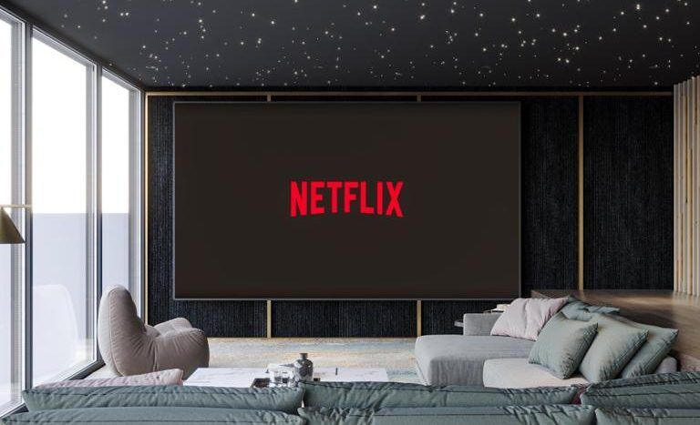 Une salle de cinéma maison moderne dans une villa de Dubaï avec des murs sombres, un plafond éclairé par des étoiles et un grand écran affichant le logo Netflix. La chambre dispose de coussins de sol et d'un long canapé.