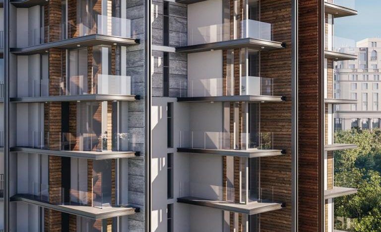 Vue rapprochée d'une façade d'immeuble d'appartements moderne comportant une colonne centrale recouverte de bronze flanquée de balcons avec balustrades en verre et murs extérieurs en pierre à Dubaï.