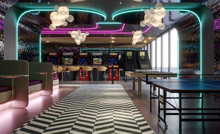 Une salle d'arcade moderne à Dubaï avec un intérieur vibrant, avec un sol à motifs de chevrons noirs et blancs, des lumières vert néon traçant les contours du plafond et des suspensions en grappe. Des machines d’arcade bordent le mur du fond.