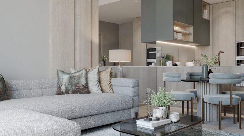Un salon élégant avec un canapé sectionnel gris moelleux, une table basse avec plateau en verre, un tapis bleu sarcelle, une cuisine moderne attenante et un luminaire circulaire doré. Les tons neutres et les textures luxueuses dominent l'esthétique