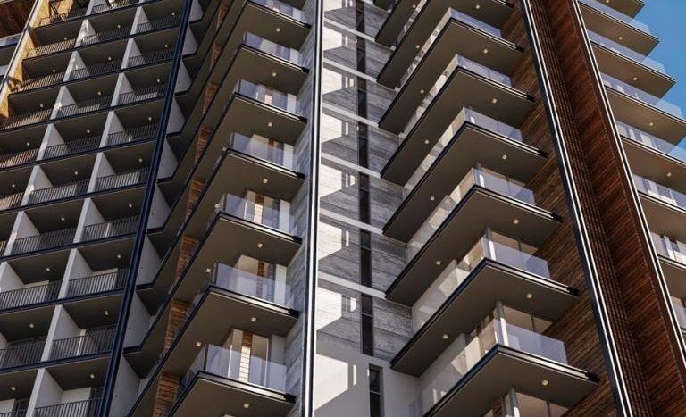 Un immeuble d'appartements moderne de grande hauteur avec balcons, présentant un mélange d'éléments de façade en bois et en métal sous un ciel bleu clair, entouré de palmiers à Dubaï.