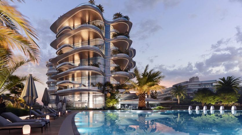 Un bâtiment moderne de plusieurs étages avec des balcons incurvés, entouré de palmiers et éclairé au crépuscule. Il y a une grande piscine au premier plan avec des chaises longues autour, mettant en valeur le premier immobilier.