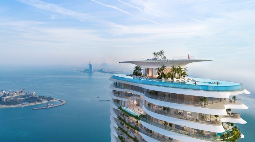 Un luxueux hôtel à plusieurs niveaux doté d'une piscine sur le toit entourée de palmiers, surplombant l'horizon brumeux de Dubaï au bord de la mer.