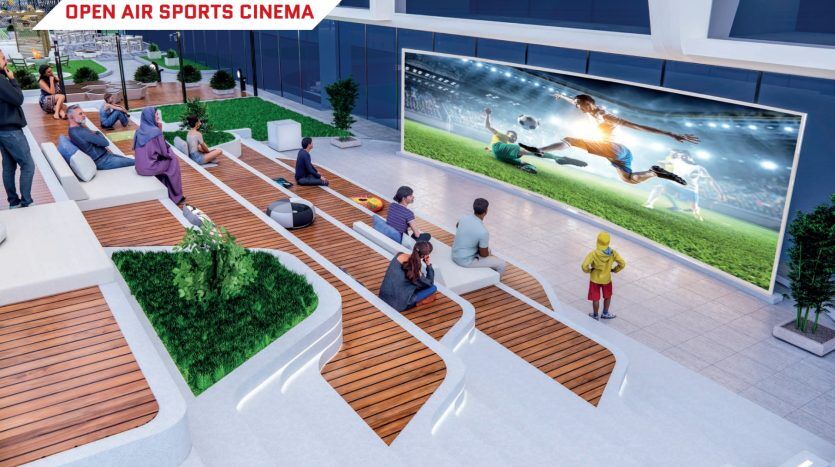 Les gens regardent un film dans un cinéma sportif en plein air doté de grands écrans diffusant un match de football, assis sur des bancs en bois à plusieurs niveaux au milieu d'une verdure luxuriante, mis à disposition par une agence immobilière de Dubaï connue pour ses équipements luxueux.