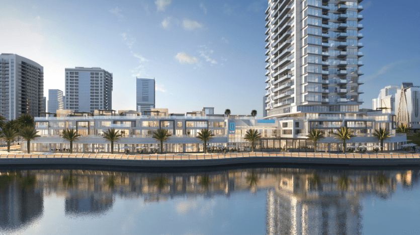 Une scène ensoleillée au bord de l'eau à Dubaï avec des immeubles de grande hauteur modernes se reflétant dans un plan d'eau calme, entouré de palmiers et d'un ciel bleu clair.