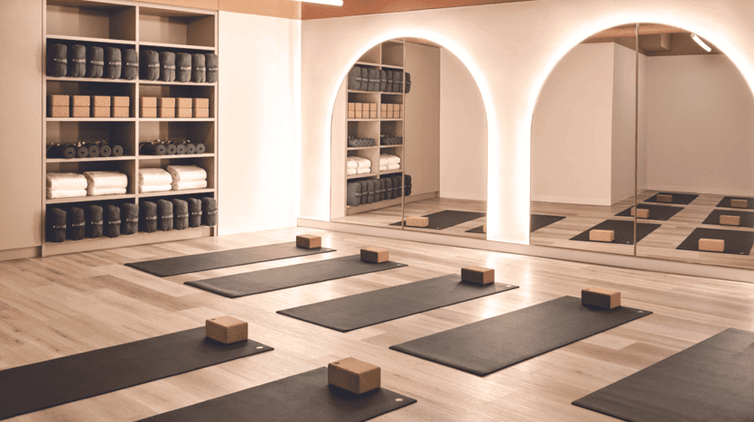 Un studio de yoga spacieux et moderne avec du parquet, des tapis et des blocs de yoga noirs et des portes cintrées menant à une étagère murale remplie de tapis de yoga roulés est un investissement idéal à Dubaï.