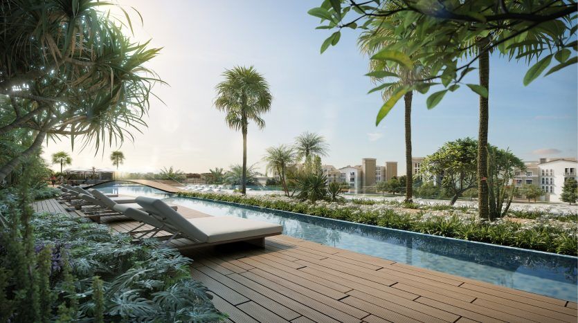 Un cadre serein au bord de la piscine avec une terrasse en bois, des chaises longues, des plantes vertes luxuriantes et des palmiers, surplombant les résidences de villas modernes de Dubaï au coucher du soleil.