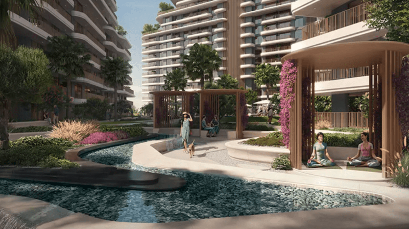 Un complexe d'appartements moderne, Verdes, dispose d'une cour luxuriante traversée par un ruisseau. Les gens se détendent dans des kiosques au milieu de la verdure et des fleurs. Deux individus pratiquent le yoga sur des tapis, tandis qu’une autre personne marche à proximité. De grands immeubles avec balcons entourent ce quartier serein.