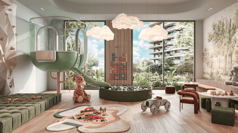 Une salle de jeux moderne pour enfants à Verdes comprend un toboggan et une zone d'escalade avec une piscine à balles, une girafe en peluche, des tables et des chaises en bois et une grande fenêtre avec vue sur l'extérieur. De doux plafonniers en forme de nuage et un décor ludique créent une atmosphère fantaisiste.