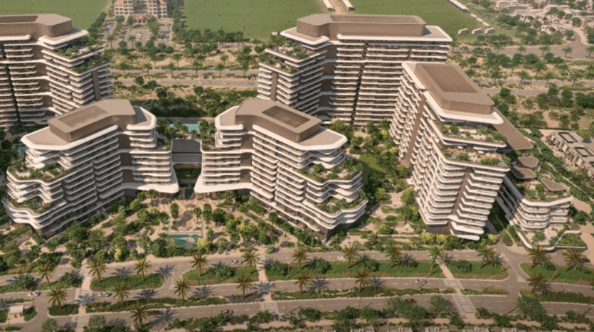 Vue aérienne d'un complexe résidentiel moderne comprenant plusieurs bâtiments à plusieurs étages dotés de balcons spacieux, entourés d'une verdure luxuriante, de palmiers et d'allées paysagées. Le complexe Verdes est situé à proximité de champs ouverts et de routes, présentant une conception urbanistique.