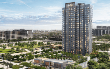 Un immeuble de grande hauteur labellisé « HYDE Residences » se dresse au milieu d'une verdure luxuriante et d'une architecture moderne. La zone environnante comprend des espaces verts, des arbres et des structures de faible hauteur, situés sous un ciel partiellement nuageux avec un paysage urbain tentaculaire et des bâtiments lointains en arrière-plan.