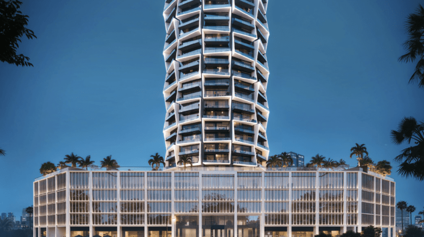 Un immeuble moderne de grande hauteur à l'architecture torsadée, avec des arêtes illuminées. Les niveaux inférieurs ont une façade en forme de grille et des toits verdoyants avec des palmiers, le tout dans un ciel clair.