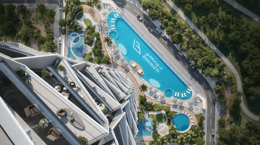 Vue aérienne d'une piscine moderne sur le toit, avec des chaises longues, des zones ombragées et de la verdure, entourée d'un bâtiment au design unique et adjacente à une route bordée d'arbres.