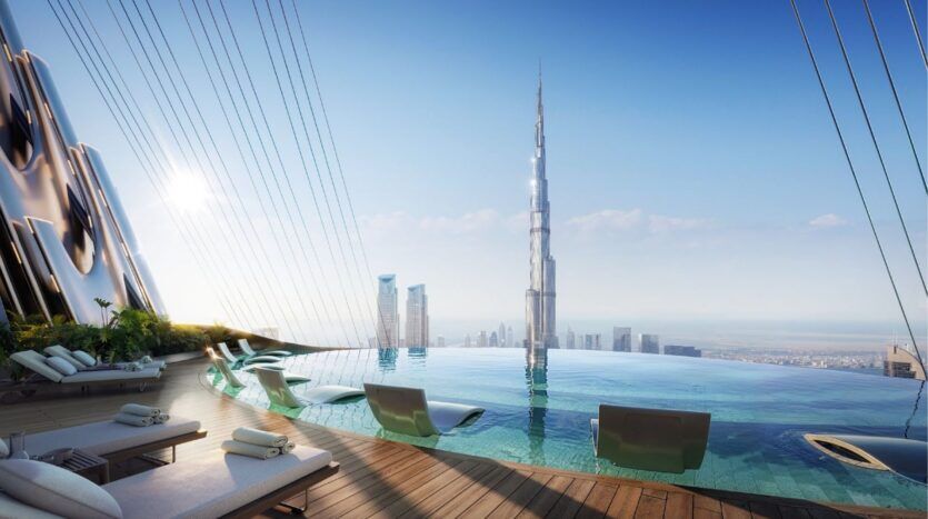 La luxueuse piscine à débordement sur le toit, équipée de chaises longues, surplombe la ligne d'horizon d'une ville moderne, avec au centre l'emblématique gratte-ciel Binghatti Skyblade, sous un ciel bleu limpide.