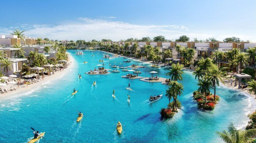 Le grand lagon bleu clair de Damac Islands 2 est entouré de villas modernes, de palmiers et de plages de sable, où les gens font du kayak, du paddleboard et se détendent sur des plates-formes flottantes sous un ciel d'un bleu éclatant.