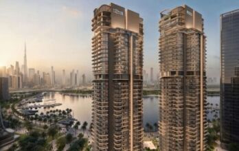 Deux tours modernes portant des panneaux "Creek Waters" mettent en valeur l'art architectural en surplombant un port de plaisance et une promenade bordée de palmiers, avec l'horizon de la ville et la Burj Khalifa visibles en arrière-plan au coucher du soleil.