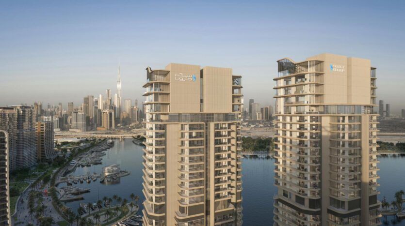 Deux gratte-ciel modernes mettent en valeur l'art architectural en surplombant un port de plaisance parsemé de bateaux et de palmiers, tandis que la silhouette de la ville et l'emblématique Burj Khalifa s'élèvent à l'arrière-plan, sous un ciel dégagé.