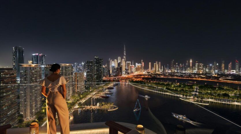 Une femme se tient sur un toit-terrasse la nuit, surplombant la ligne d'horizon d'une ville moderne dont les gratte-ciel illuminés au bord d'une rivière témoignent de l'art architectural. Des bateaux naviguent sur l'eau, reflétant les lumières vibrantes de la ville.