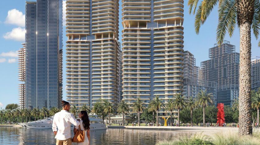 Un couple se tient au bord de l'eau, admirant les gratte-ciel modernes aux balcons arrondis, les palmiers, les yachts amarrés à proximité et les sculptures d'art public vibrantes qui mettent en valeur l'art de la ville dans un cadre urbain ensoleillé.