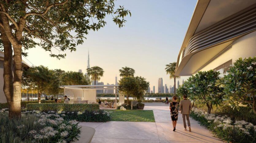 Un couple marche le long d'un sentier aménagé dans un parc moderne, entouré d'une végétation luxuriante et de palmiers. Les gratte-ciel de la ville, dont le Burj Khalifa, s'élèvent à l'horizon au coucher du soleil.