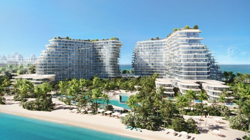 Les deux tours modernes et vitrées de Bella by Passo s'élèvent au-dessus des palmiers et des jardins, surplombant une superbe plage de sable blanc et une eau turquoise. Des piscines, des parasols et des chaises longues sont installés près du rivage, sous un ciel bleu clair.
