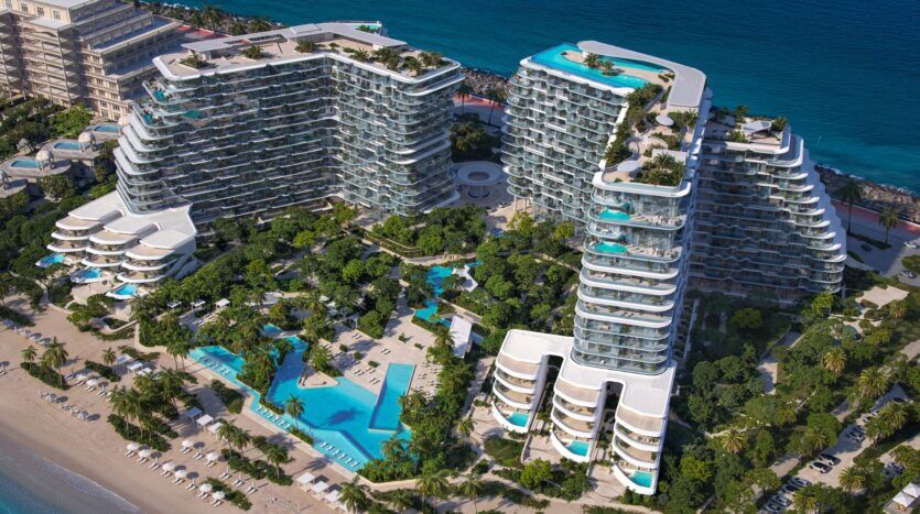 Vue aérienne de Bella by Passo, un grand complexe moderne en bord de mer avec des bâtiments aux murs de verre incurvés, de nombreuses piscines, des palmiers luxuriants et des espaces de détente, le tout surplombant l'océan turquoise.