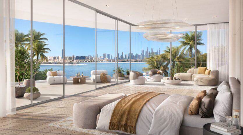 Une luxueuse chambre à coucher Bella by Passo avec des fenêtres allant du sol au plafond s'ouvre sur un balcon spacieux avec des sièges modernes, avec vue sur les palmiers, l'eau et la ligne d'horizon de la ville au loin sous un ciel clair et lumineux.