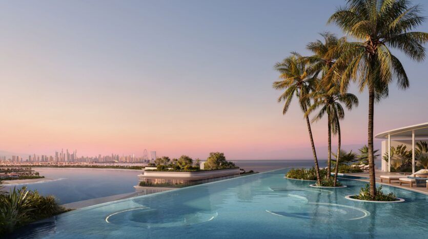 Piscine à débordement avec des sièges circulaires et des palmiers à Bella by Passo, surplombant l'océan et l'horizon lointain de la ville au coucher du soleil. Le ciel rose et violet crée une atmosphère tranquille et luxueuse.