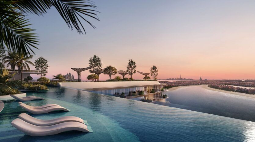 La piscine à débordement et les chaises longues blanches de Bella by Passo surplombent une rivière pittoresque et l'horizon de la ville au coucher du soleil ; des palmiers et des structures de jardin modernes bordent la terrasse, créant une atmosphère luxueuse et tranquille.