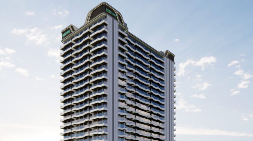 Un grand immeuble moderne, Reef 996, avec de nombreux balcons et baies vitrées, se dresse sur un ciel bleu parsemé de nuages. La structure présente des angles incurvés et des panneaux de signalisation sur le toit.