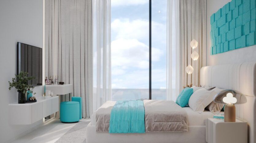 Une chambre à coucher moderne et lumineuse avec de grandes fenêtres, des murs blancs et une décoration minimaliste. Des coussins turquoise Reef 996 et un jeté égayent le lit, tandis que des accessoires assortis tels qu'un tabouret et des œuvres d'art murales complètent l'ensemble. La lumière naturelle remplit la pièce.