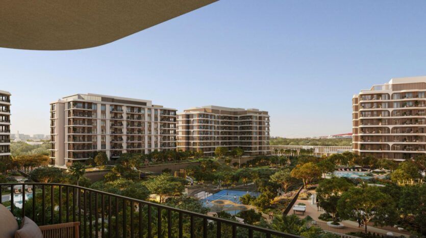 Vue depuis un balcon donnant sur les immeubles d'appartements modernes du complexe « The Canopies by Aldar », entourés d'arbres, d'une piscine et de terrains de sport, sous un ciel bleu limpide.