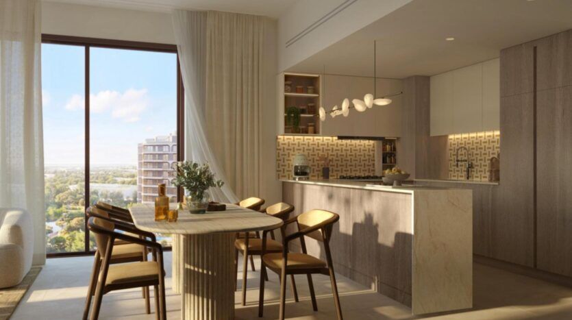 Cuisine et coin repas modernes aux finitions en bois et en marbre au complexe « The Canopies by Aldar », comprenant six chaises disposées autour d'une table, de grandes baies vitrées offrant une vue sur la ville et la verdure, ainsi que des suspensions au-dessus de l'îlot central.
