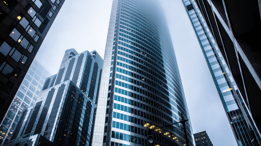 Vue depuis le niveau de la rue des gratte-ciel imposants sous un ciel nuageux, avec un bâtiment reflétant bien l'atmosphère couverte, entouré d'autres structures de grande hauteur idéales pour investir à Dubaï.