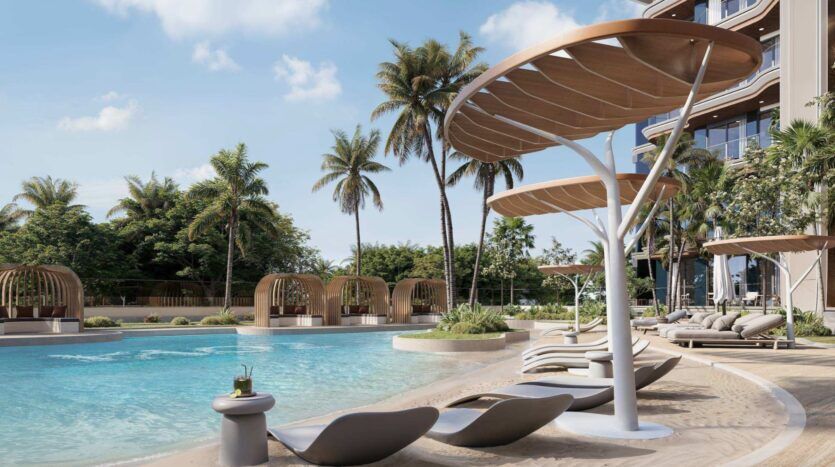 L'espace luxueux au bord de la piscine du Mirari Lagoon by Zoya propose des chaises longues modernes, de grands auvents en forme de feuille, des palmiers et des cabines privées, le tout situé à côté d'un superbe bâtiment de complexe hôtelier, sous un ciel ensoleillé.