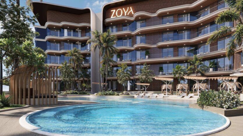 Un hôtel moderne, avec ses balcons incurvés, ses palmiers et sa grande piscine extérieure, invite ses clients à profiter d'un havre de paix au Mirari Lagoon by Zoya. Des transats et des coins salon ombragés entourent la piscine, tandis que le bâtiment arbore en son sommet une enseigne « ZOYA » bien visible.