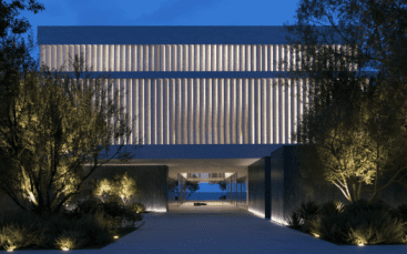Bâtiment moderne de Dubaï éclairé au crépuscule avec un design symétrique comportant une passerelle centrale menant sous une grande structure surélevée flanquée de rangées d'arbres.